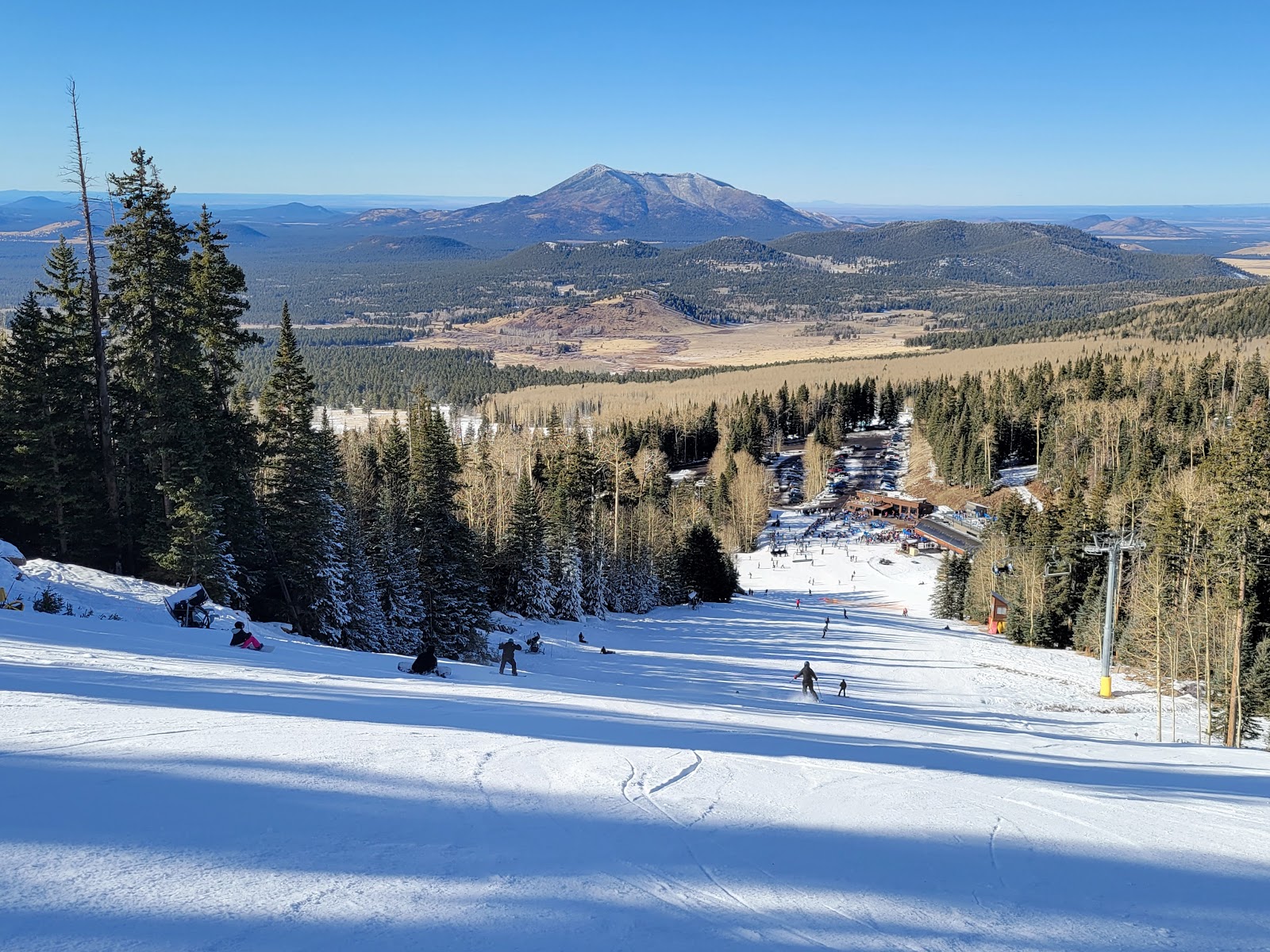 Skiers on a sunny groomed run with desert views beyond