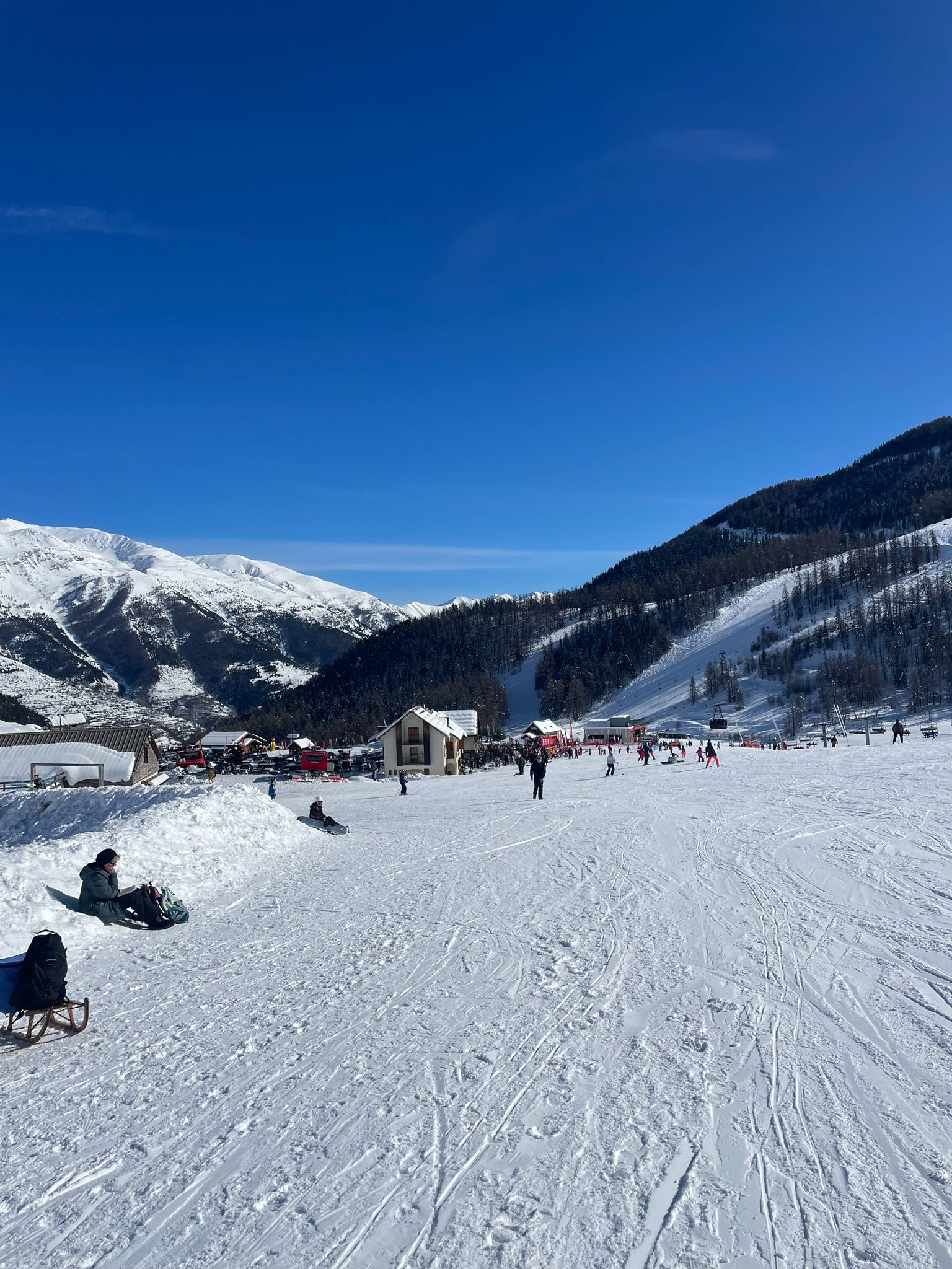 Skiers on a wide sunny run with southern Alpine views at Auron