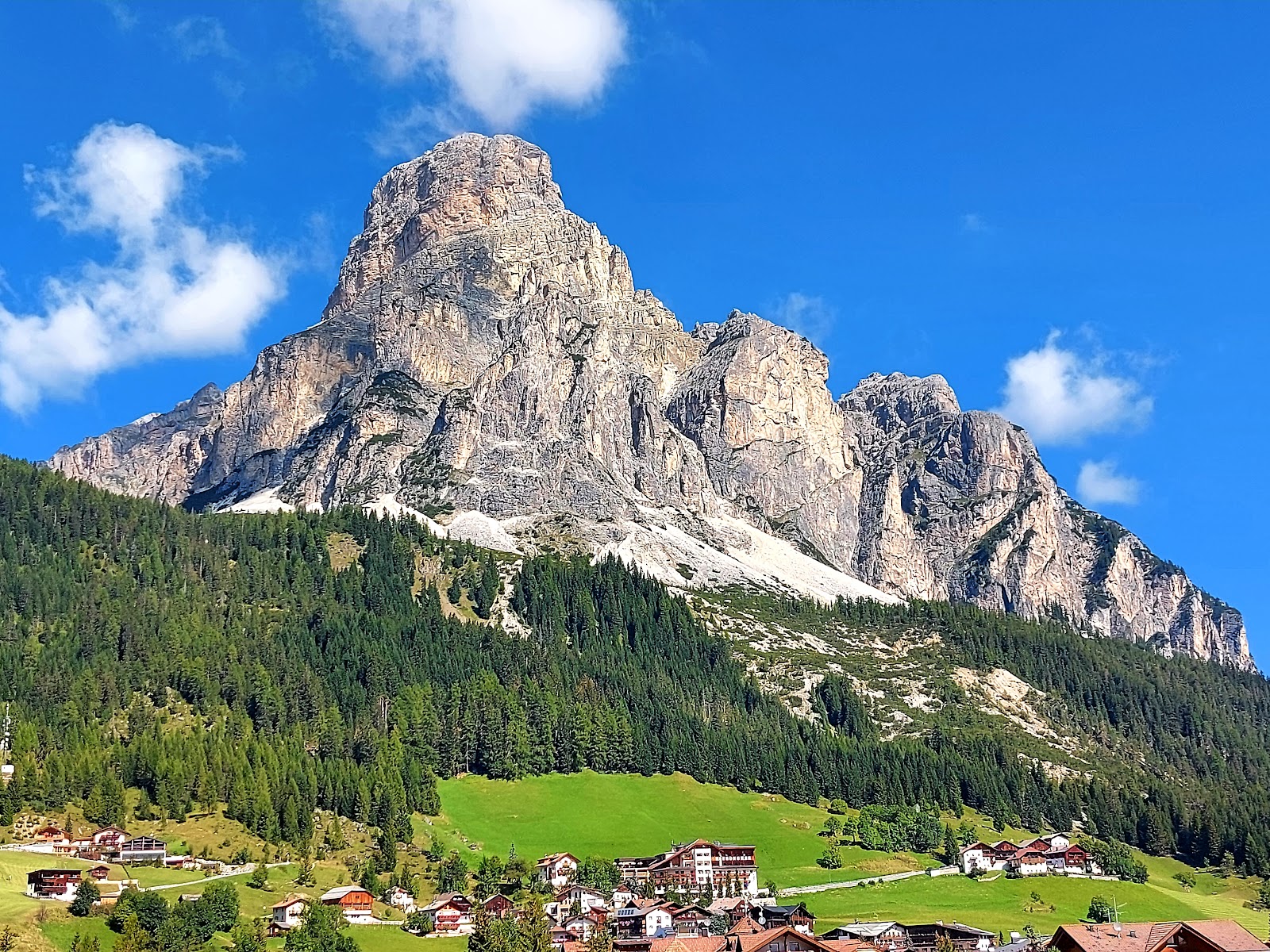A wide sunny groomed piste beneath dramatic Dolomite rock walls