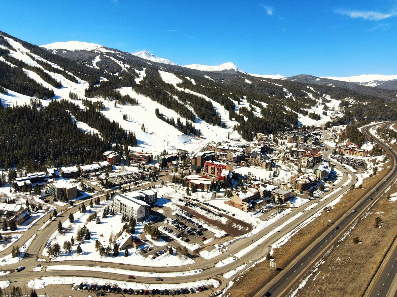 Skiers descending a wide groomed blue run at Copper Mountain in sunshine