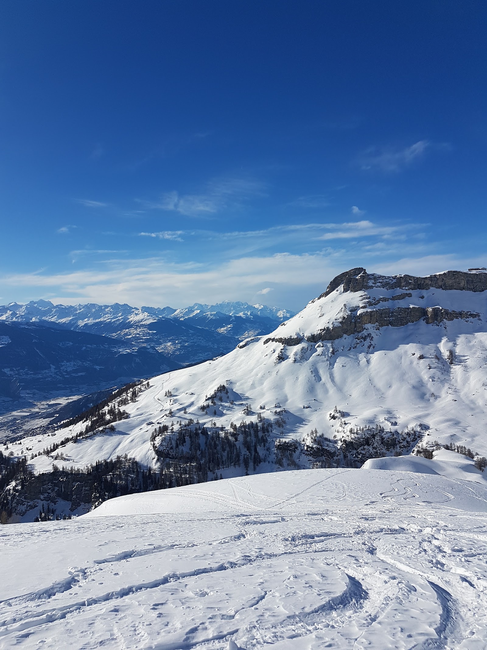 Wide sunny ski pistes above Crans Montana looking across the Rhone valley to the high Valais peaks