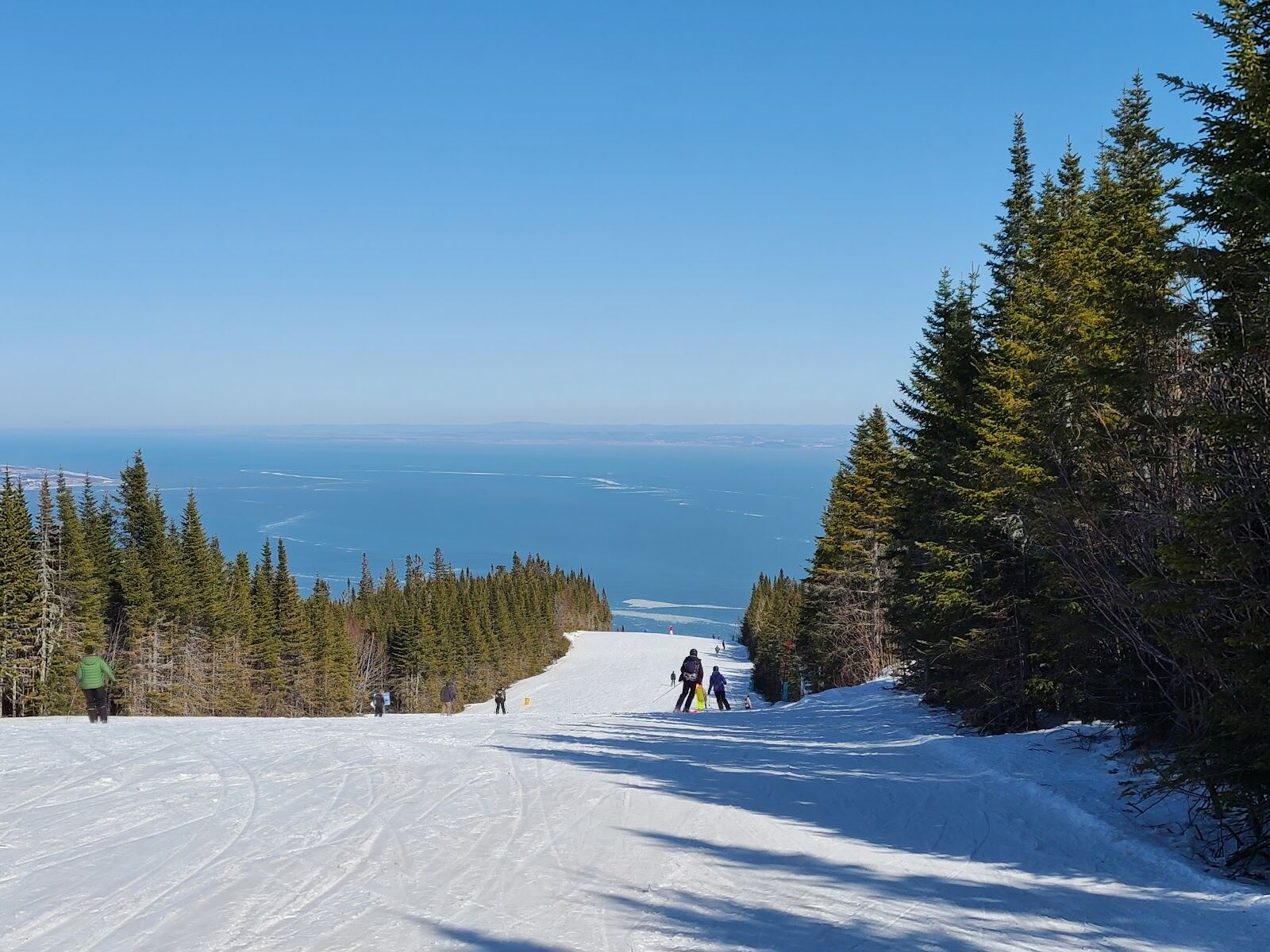 Skiers on a groomed slope with the frozen river far below at Le Massif