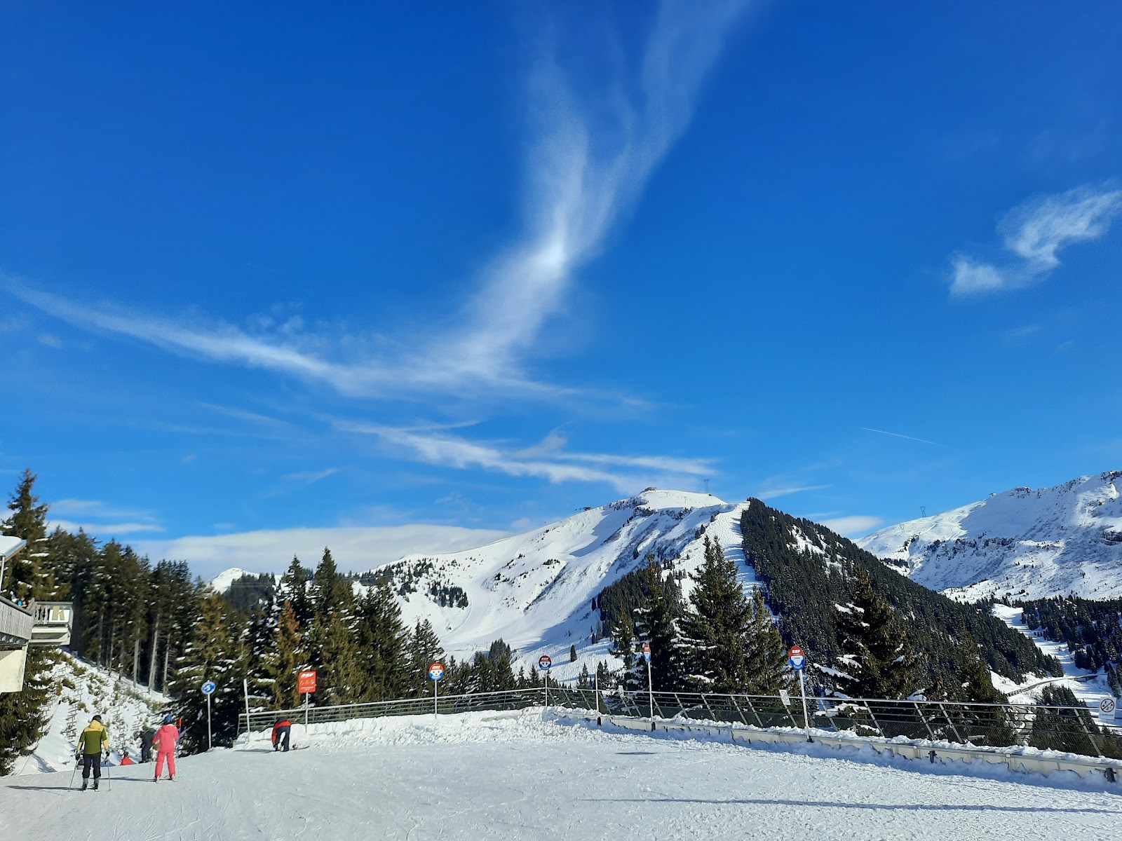 Skiers on a wide blue run with valley views at Les Carroz
