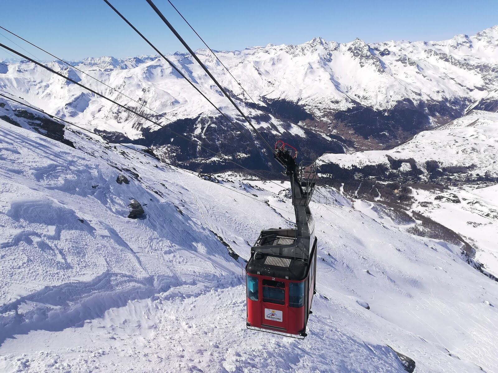 Skiers on a sunny groomed run with the Valtellina peaks beyond