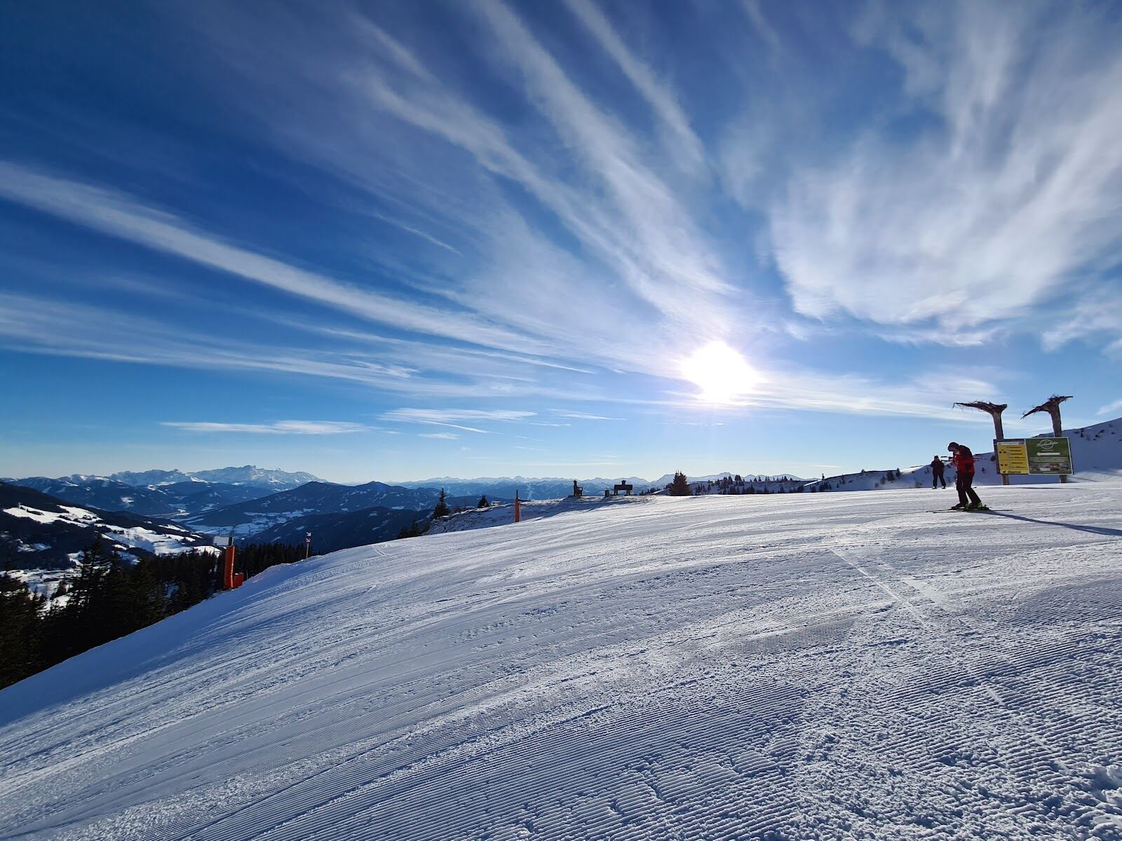 Skiers on a wide groomed run with the Hochkonig massif beyond