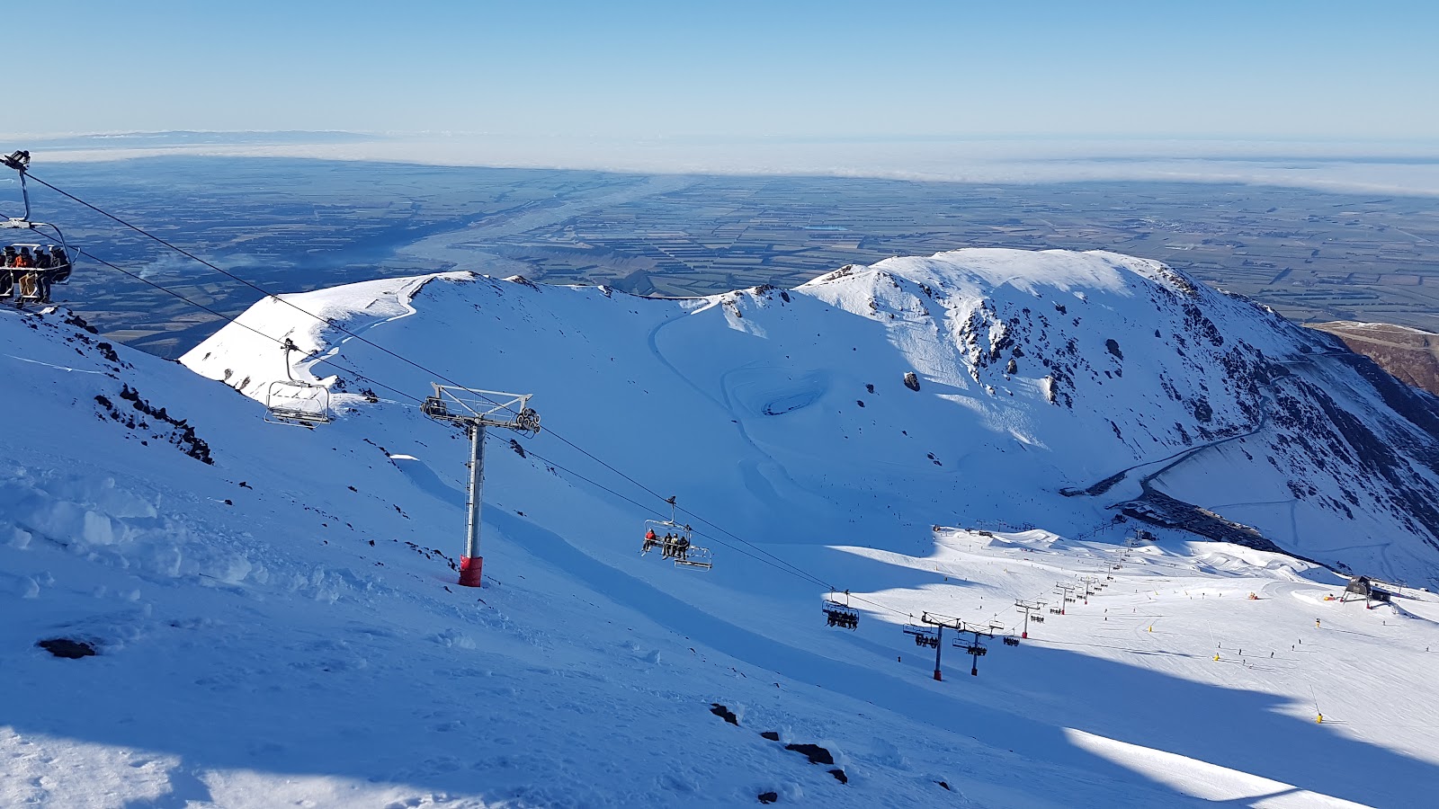 Skiers on a groomed run with views over the Canterbury plains from Mt Hutt
