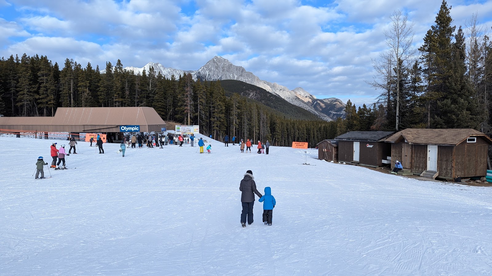 A chairlift climbing a groomed snowy Alberta mountain on a sunny day at Nakiska