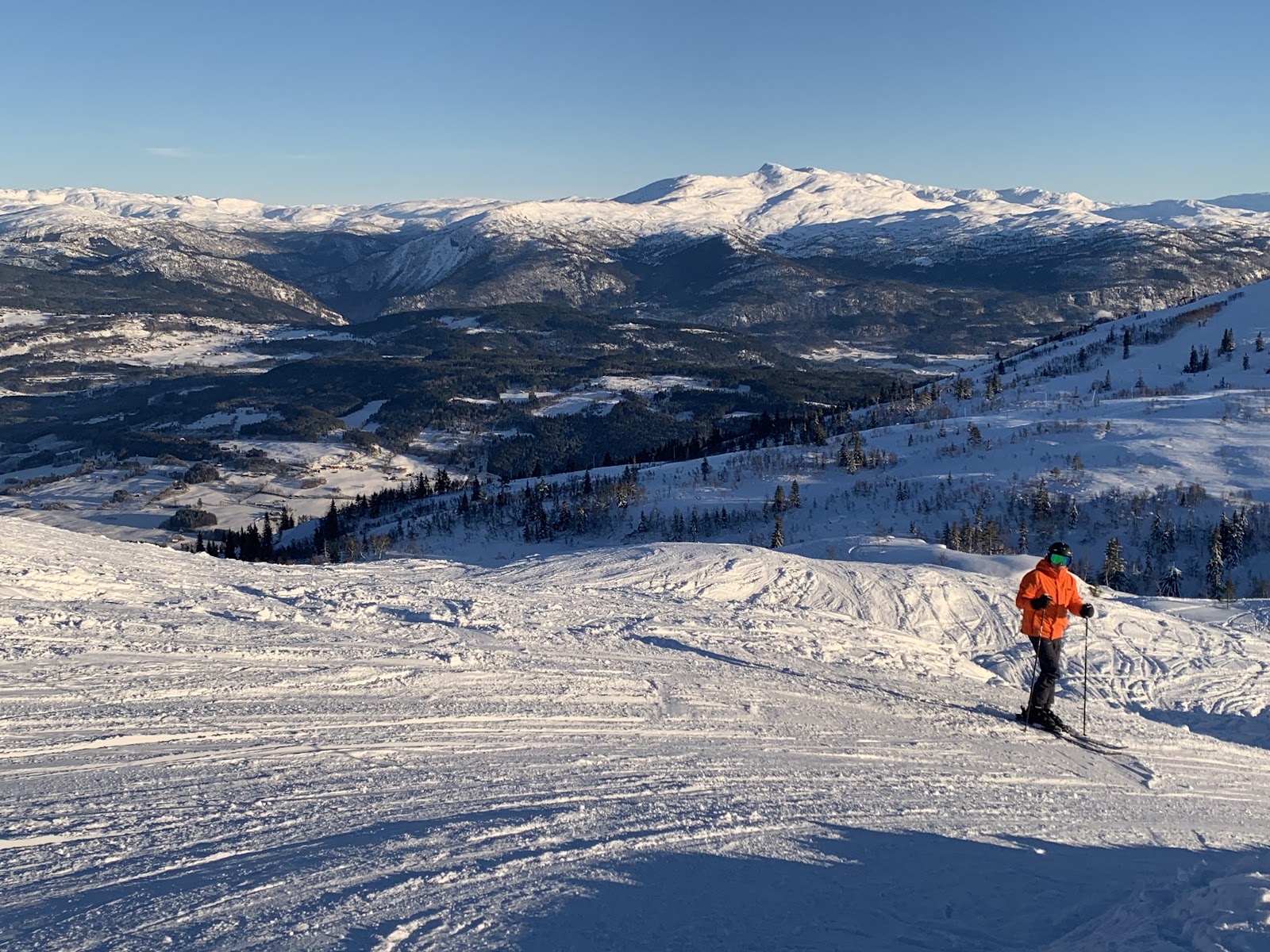 Skiers on a wide piste with Norwegian fjord country beyond
