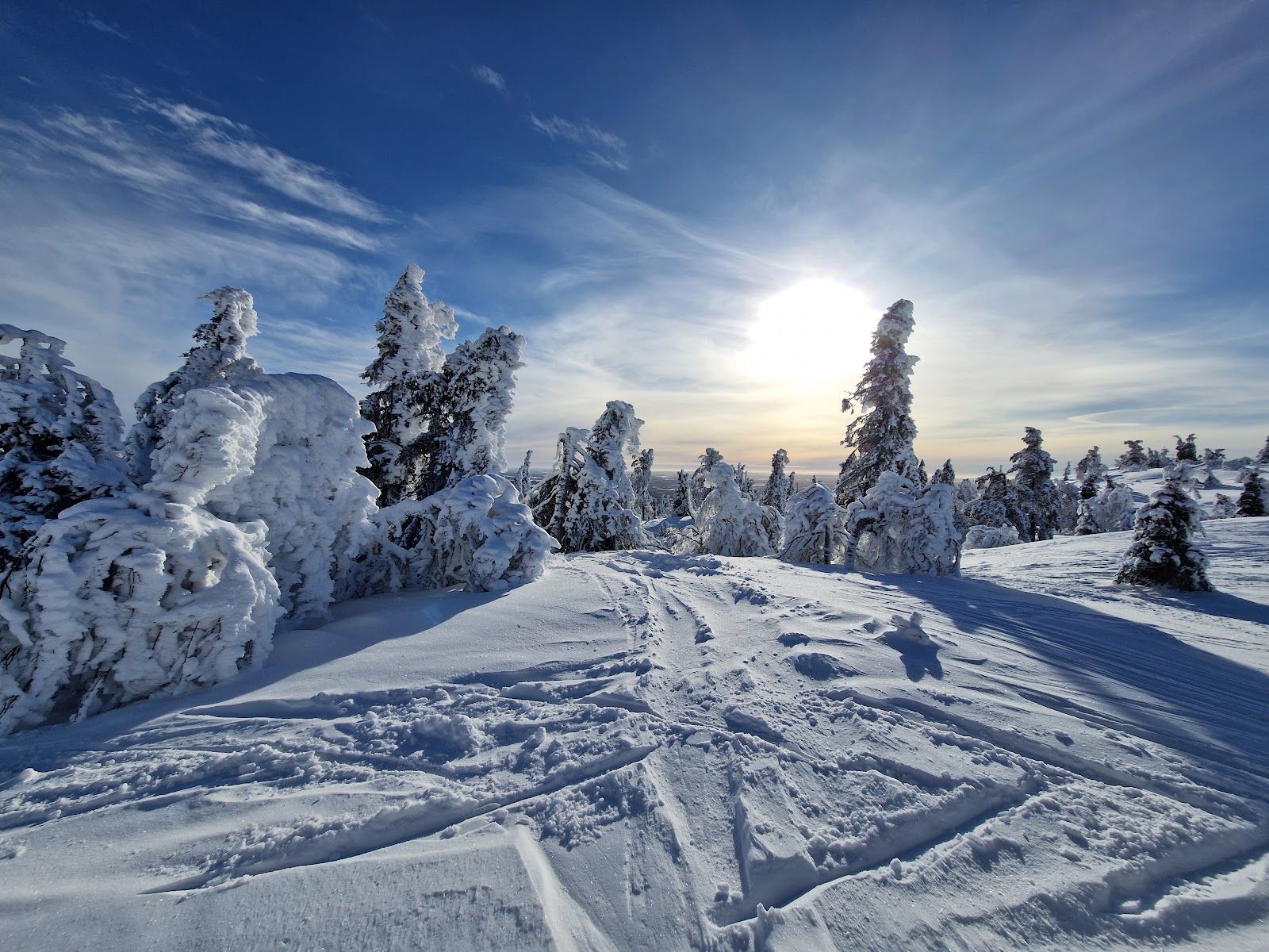 Skiers riding a chairlift over a wide white fell in soft light